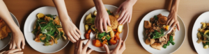 Overhead view of hands reaching for plates of vegetables, grains, and greens at a shared meal centered on the microbiome diet