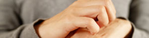 Person in a grey sweater scratches dry, itchy skin from hand eczema